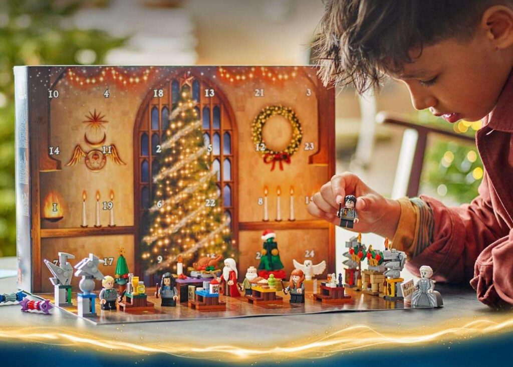 Child placing a minifigure into a LEGO-style advent calendar scene with numbered doors and a lit Christmas tree backdrop