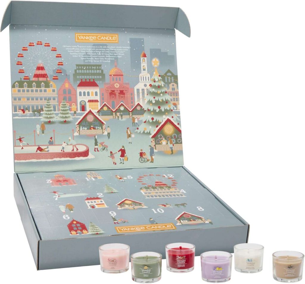 Open illustrated winter-village advent calendar box with numbered doors and six small scented votive candles lined in front.