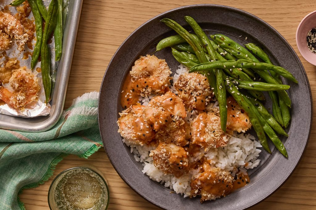 Bowl of rice topped with crispy panko shrimp drizzled in sauce served with sautéed green beans and sesame
