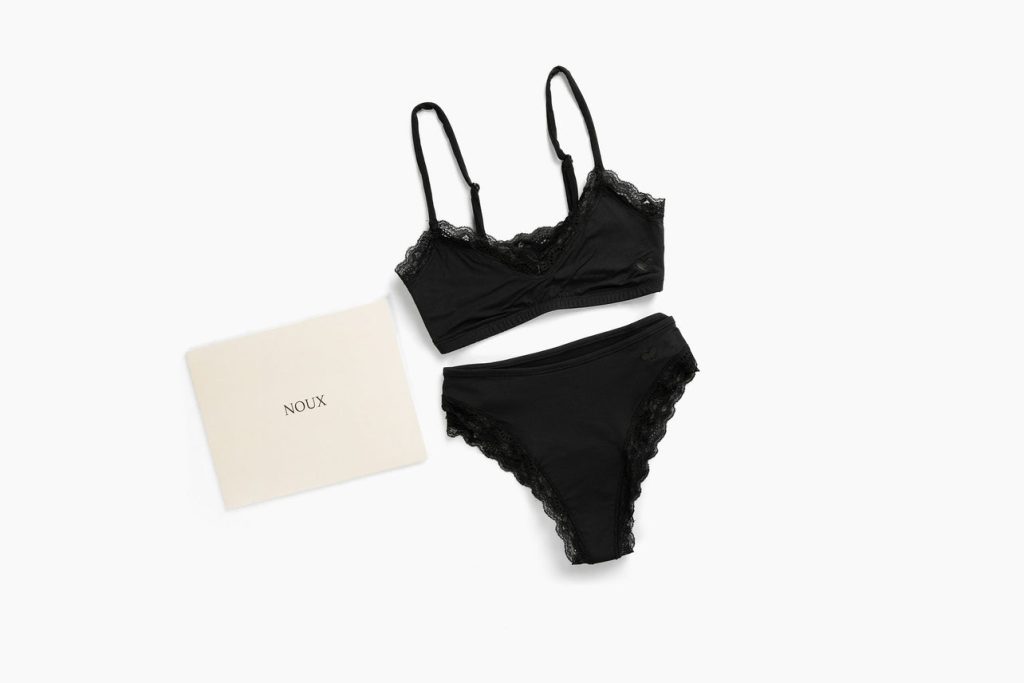 Black lace-trimmed bralette and matching high-waisted panties displayed alongside a cream-colored packaging envelope.