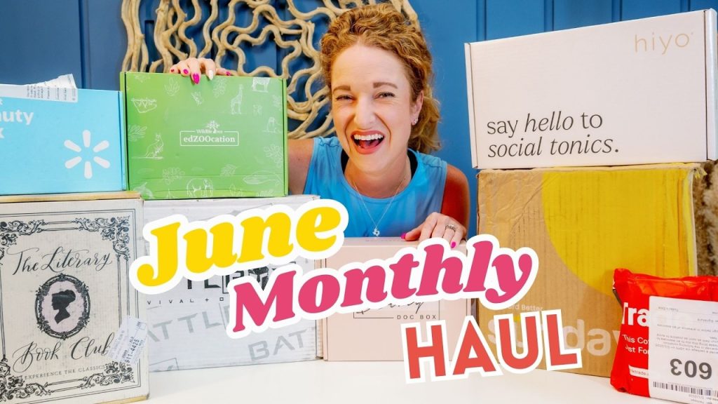 A person joyfully showcasing a variety of subscription boxes labeled for a June monthly haul, highlighting diverse products a